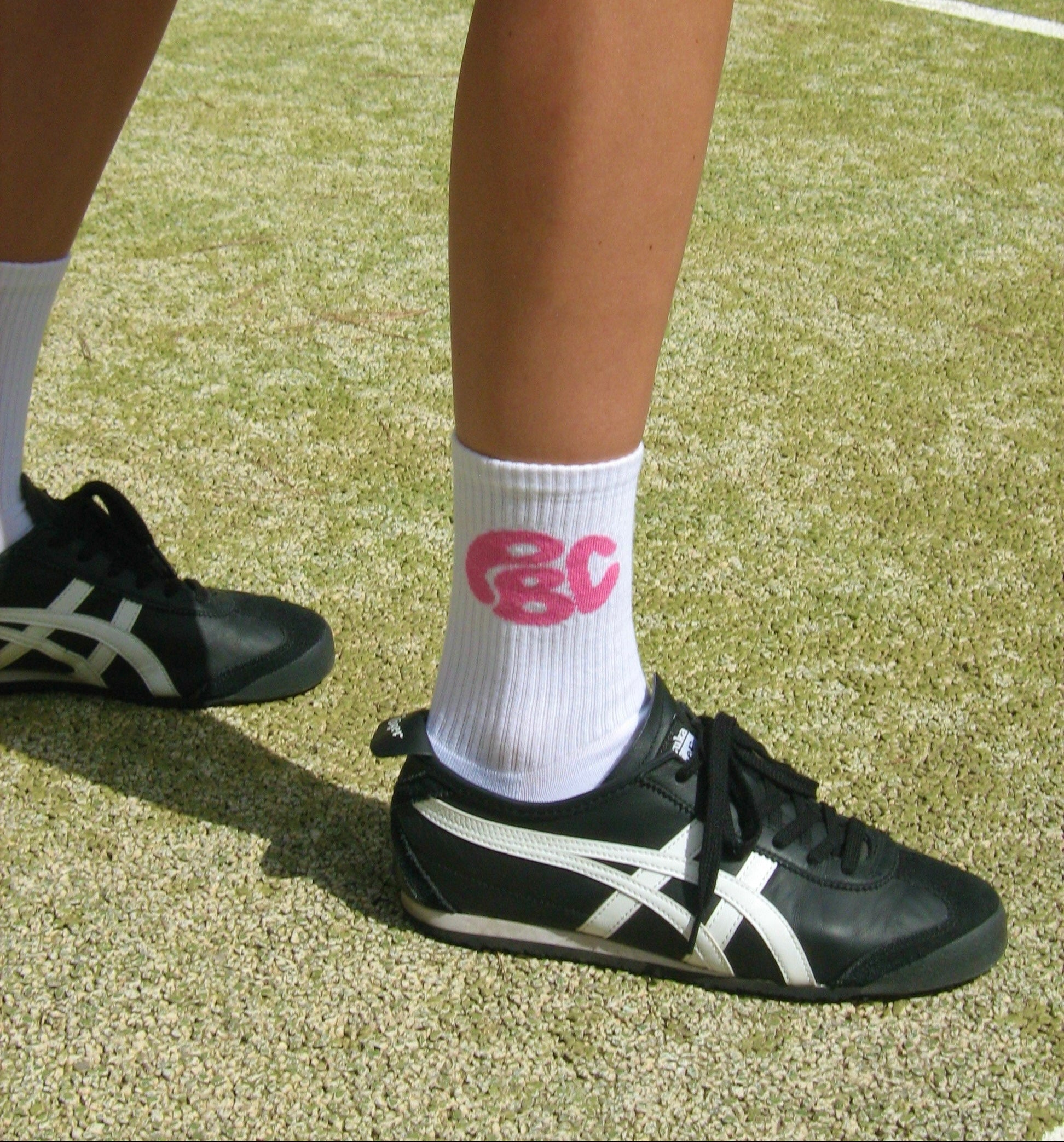 Leg from a person standing on a pickleball court wearing the Collective Socks with pink PBC Logo